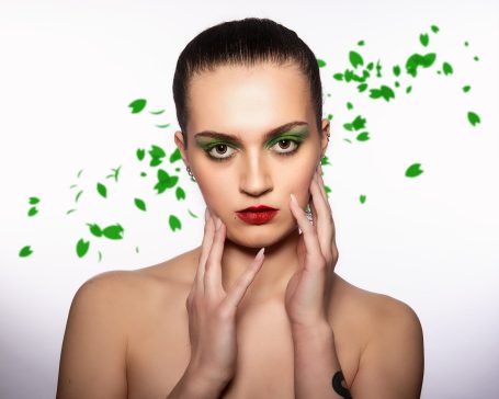 Porträt einer Frau mit grünem Augen-Make-up und roten Lippen, umgeben von grünen Blütenblättern.